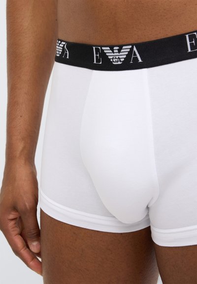 Άσπρα βαμβακερά ανδρικά εσώρουχα τύπου μποξέρ με μαύρη ελαστική μέση που έχει λογότυπο. Ομαλή υφή και εφαρμοστή σχεδίαση, εμφανιζόμενα από το πλάι.