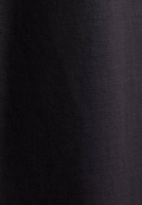 Gros plan sur un tissu noir foncé avec une texture tricotée visible et un éclairage subtil montrant de fins fils et une surface lisse.