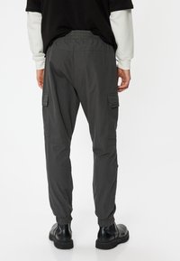 Grijze cargo broek met elastische tailleband, enkelboorden en twee zijzakken; heeft een gestructureerde stof met een subtiel patroon.