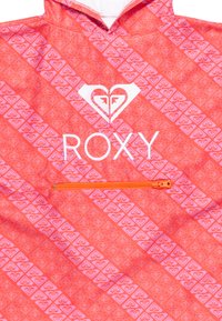 Roxy windbreaker in bright coral with pink geometric heart pattern. Features a white logo and an orange zippered pocket. Lightweight material.