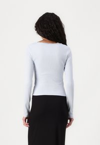 Light blue long-sleeve top with ribbed texture and delicate lace trim at the neckline, paired with a black skirt.