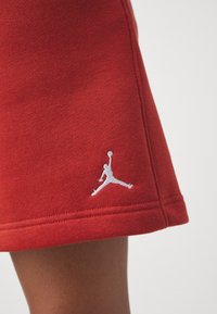 Sweatshirt rouge en matériau doux, avec un logo Jumpman blanc sur l'ourlet. Texture agréable avec des coutures visibles.