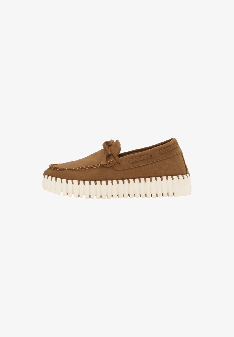 Bruine suède moccasin-stijl schoen met een witte gegroefde zool, een decoratieve strik en zijkanten met uitsparingen voor ventilatie.