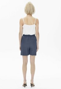 Vit linne med tunna band, kombinerat med mörkblå shorts med elastisk midja, sedd bakifrån. Slätt, lätt tyg.