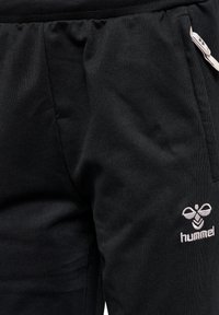 Zwarte sportbroek van textiel met een gestructureerde stof, voorzien van een elastische tailleband en een zijzak met rits. Het Hummel-logo is in het grijs geborduurd.