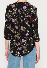 Blusa nera con stampa floreale colorata, maniche a tre quarti, orlo arrotondato e dettaglio plissettato sul retro. Tessuto dalla texture liscia.