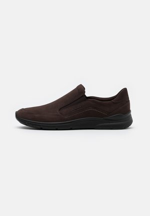 Bruine herenslip-on casual schoen met zwarte zool en subtiele stiksel details, getoond vanaf de buitenzijde op een witte achtergrond.