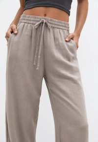 Světlé béžové široké kalhoty vyrobené z texturované tkaniny, s elastickým pasem na šňůrku a bočními kapsami.