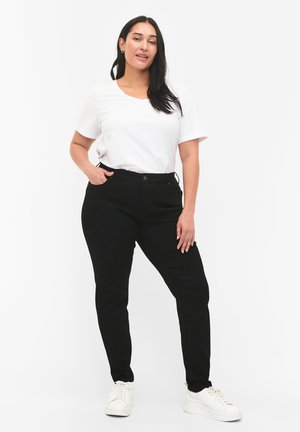 Pantalon noir à coupe slim avec poches avant, associé à un t-shirt blanc simple à manches courtes et des baskets blanches.