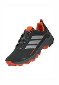 Czarno-pomarańczowe buty na zewnątrz z cholewką Gore-Tex, trzema szarymi paskami, teksturową powierzchnią, trwałą podeszwą i systemem sznurowania.