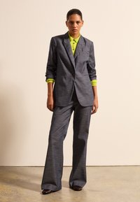 Grauer maßgeschneiderter Anzug mit weiten Hosen, kombiniert mit einem neongrünen Kragenhemd. Glatte Stofftextur; strukturierter Blazerstil.