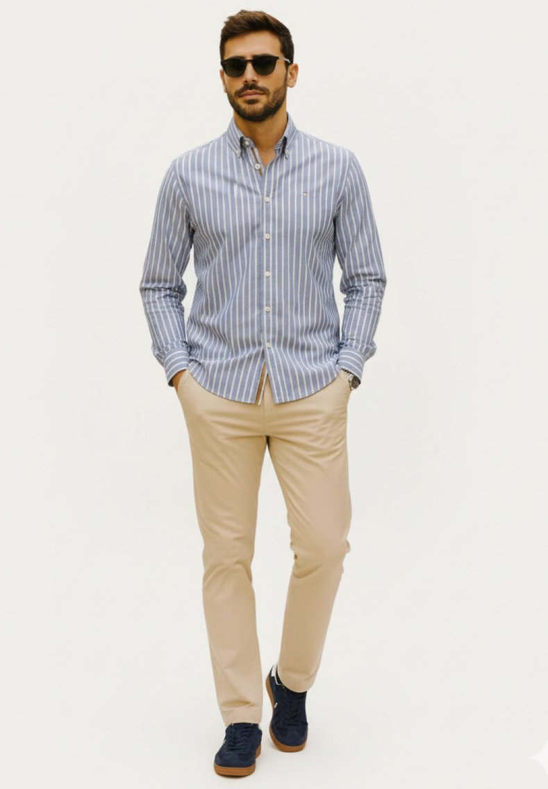 Camisa de botones a rayas azul claro y blanca, pantalones beige y zapatos navy. El modelo lleva gafas de sol; ajuste casual, tela suave y líneas limpias.