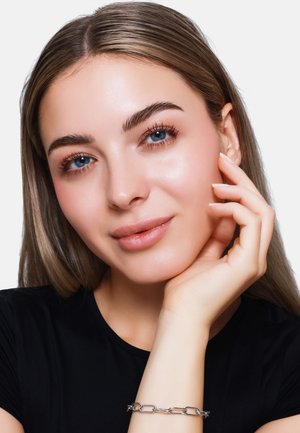 Srebrna bransoletka na nadgarstku, z owalnymi ogniwami. Modelka ma jasną skórę, proste brązowe włosy, niebieskie oczy i naturalny makijaż.