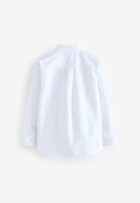 Chemise blanche à manches longues vue de dos avec des poignets boutonnés et un pli central dans le dos.