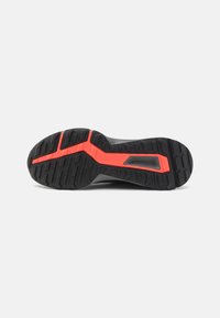 Suola di scarpa da corsa nera con superficie in gomma testurizzata, un accento rosso brillante a forma di croce e un marchio centrato.