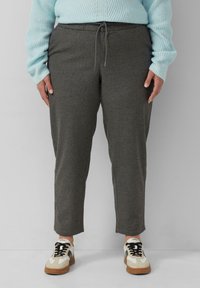 Graue Jogginghosen mit einem elastischen Bund und Kordelzug, ausgestattet mit Seitentaschen und einem schmal zulaufenden Beindesign. Getragen mit lässigen Turnschuhen.