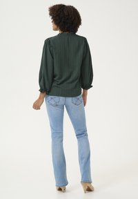 Blusa verde a righe con maniche a sbuffo, abbinata a jeans svasati blu chiaro e décolleté beige. Vista posteriore mostrata.
