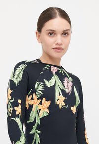Swimsuit de manga longa em preto com padrões florais vibrantes em verde, laranja e rosa. Apresenta um design ajustado com detalhes de ombro sem costura.