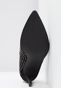Chaussure à talon haut en suède noir avec bout pointu, ornée d'accents cloutés argentés le long du côté et d'une semelle noire lisse.