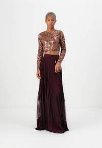 Leoaprdprint crop top med lange ermer og frontknapper, kombinert med et flytende burgunder plisséskjørt med et blondepanel nederst.
