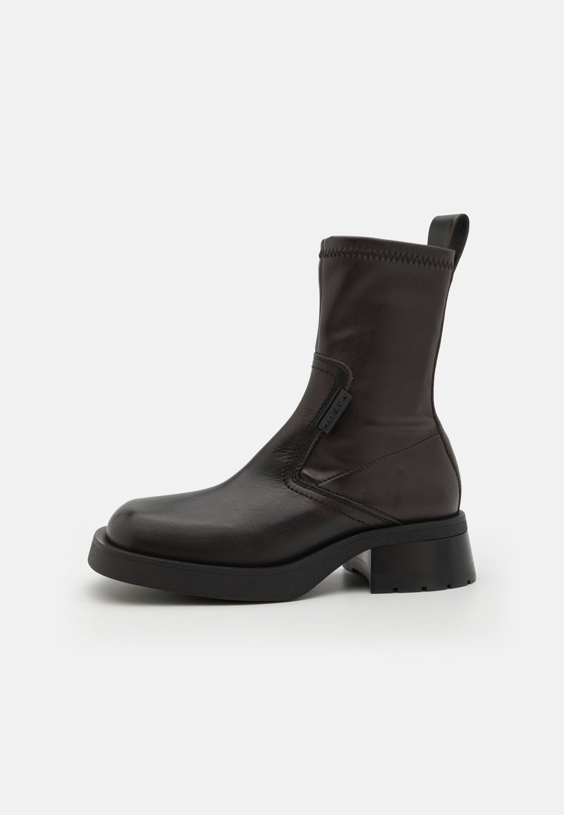 Bota de tornozelo em pele preta com textura lisa, bico redondo e um bloco resistente. Apresenta um fecho lateral e uma alça para fácil colocação.