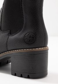 Botín de cuero negro a la altura del tobillo con paneles laterales elásticos, superficie texturizada, un tacón bloque sólido y un emblema de la marca cerca de la parte trasera.