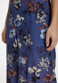 Bloemenjurk van blauwe stof met gedetailleerde patronen van witte, blauwe en rode bloemen met groene accenten. Zachte textuur en vloeiende ontwerp.