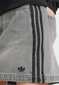 Pantalones cortos de mezclilla gris con detalles de tres franjas negras, un logo bordado y un corte clásico con bolsillos laterales.