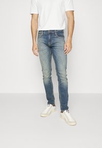 Vaqueros pitillo azul claro de tela vaquera, con un acabado desgastado y diseño de cinco bolsillos, combinados con zapatillas blancas y una camiseta blanca lisa.