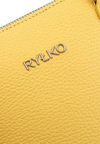 Borsa gialla in pelle con superficie texture e zip argentata. Presenta un logo "RYŁKO" argentato in evidenza sulla parte anteriore.