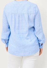 Blusa azzurra chiara a maniche lunghe in lino con vestibilità rilassata, piega arricciata sul retro e polsini con bottoni. Texture liscia, design casual.