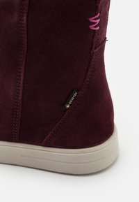 Gros plan de l'arrière d'une botte en daim bordeaux avec une semelle beige et une étiquette en tissu Gore-Tex.