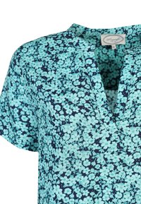 Kurzarmbluse in Marineblau mit floralem Muster in Himmelblau. V-Ausschnitt mit dezenter Knopfleiste. Leichter Baumwollstoff.