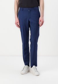 Blaue maßgeschneiderte Hose mit glatter Textur, ausgestattet mit einem Reißverschluss, Gürtelschlaufen und schmaler Passform, kombiniert mit weißen Sneakern.