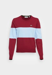 Červený a světle modrý pruhovaný svetr s dlouhým rukávem a kulatým výstřihem; vyroben z měkké pleteniny; má malé zelené logo Lacoste.