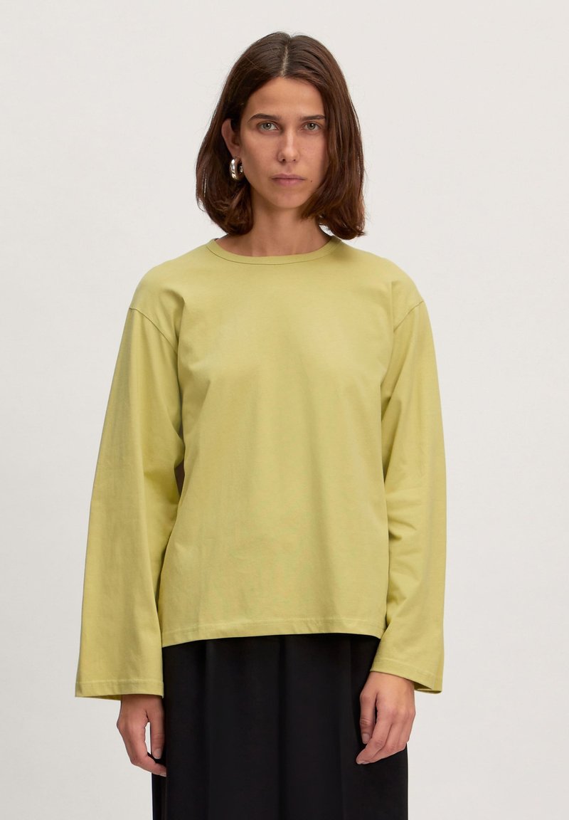 Lange mouw, ronde hals shirt in lichtgroene katoen, met een relaxte pasvorm en verlaagde schouders, gecombineerd met een donkere rok.