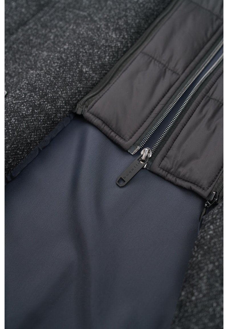 Un tessuto grigio testurizzato si combina con un rivestimento nero liscio. Presenta due tasche con zip dotate di hardware metallico e un design elegante all'interno.