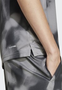 Sivá športová košeľa vyrobená z hladkej, vlhkosť absorbujúcej tkaniny s jemným motívom tie-dye. Obsahuje bočné rozparky a spevnené švy.