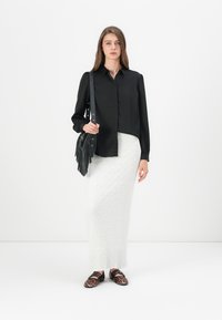 Black button-up shirt, white textured maxi skirt, black handbag with fringe, and leopard-print shoes. Clean lines and contrasting colors.