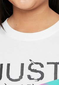 Camiseta de algodón blanca con un estampado gráfico negro y letras desgastadas. Cuello redondo y un sutil acento de degradado en la esquina inferior.