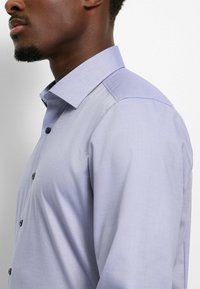 Light purple button-up shirt with a textured pattern, featuring a spread collar and dark buttons, shown from the side.