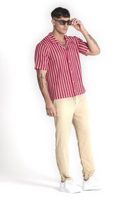 Rood-wit gestreepte short-sleeve shirt met een kraag, gedragen met beige broek en witte sneakers, zonnebril op het voorhoofd.