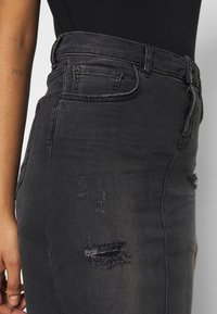 černá džínová sukně s vysokým pasem, s roztrhnutými detaily a prošíváním. Tkanina má hladkou texturu a přiléhavý střih.