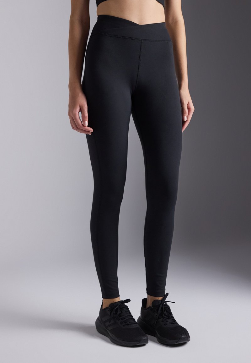 Leggings noirs en tissu extensible, dotés d'une taille haute avec un design en forme de V. Texture lisse, silhouette ajustée.