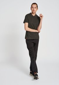 Donkergroene polo met een klassieke kraag en drie knopen, gecombineerd met zwarte tapered broeken en zwarte sneakers met rode accenten.