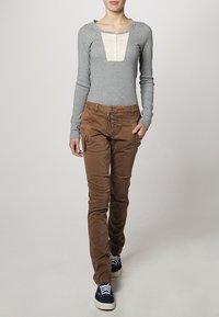 Gray long-sleeve top with a cream panel and button detail, paired with brown fitted pants featuring multiple pockets and button accents.