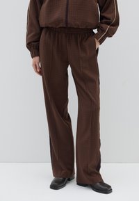 Bruine geruite broek met een elastische tailleband en zijpanelen in donkerpaars; wijde pijpen, zachte stof en discrete zijzakken.