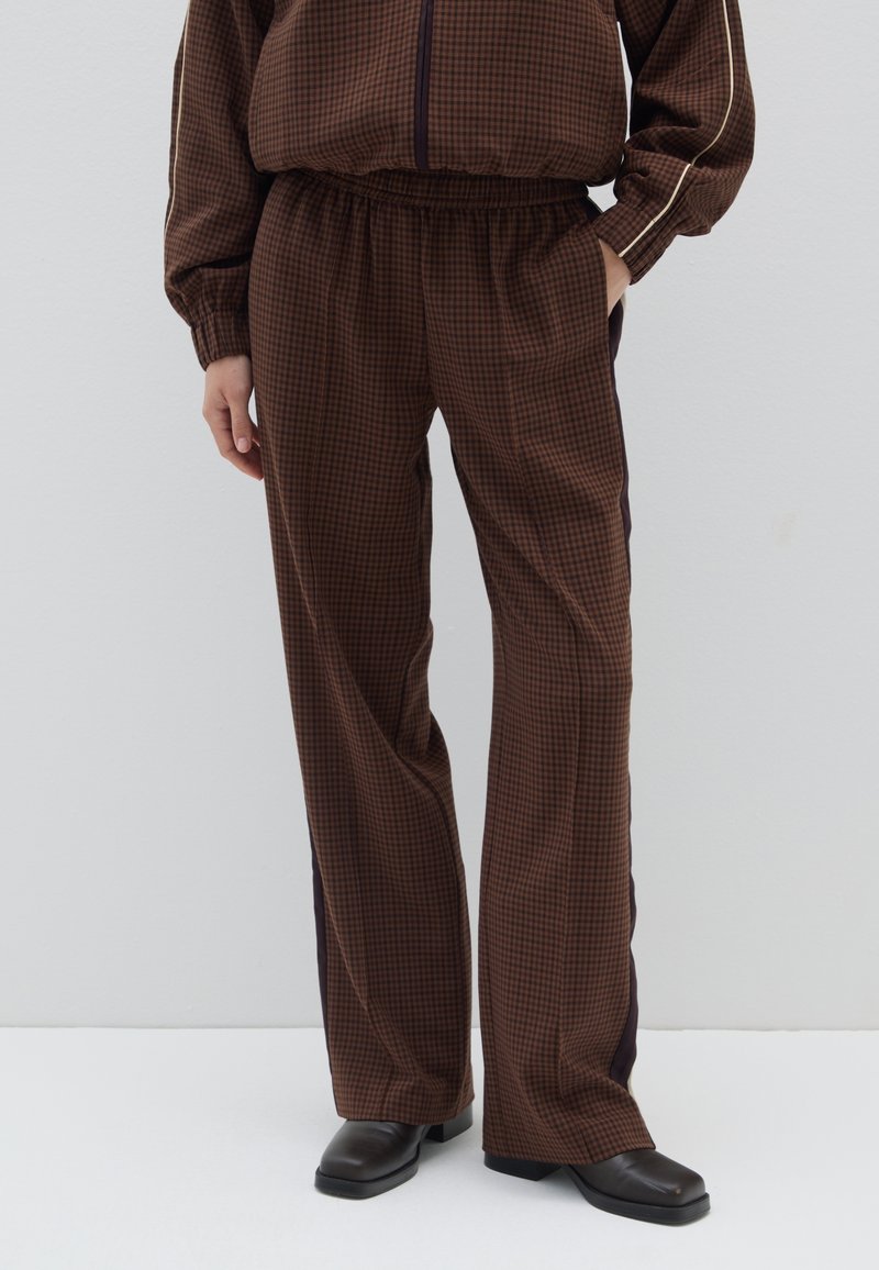 Bruine geruite broek met een elastische tailleband en zijpanelen in donkerpaars; wijde pijpen, zachte stof en discrete zijzakken.