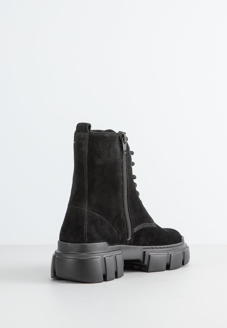 Botas de ante negro grueso con tobillo alto, cremallera lateral y suelas de goma gruesa que presentan surcos distintivos y detalles de costura.