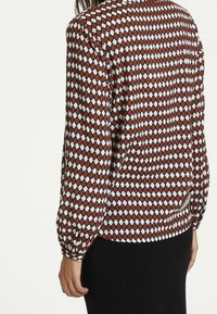 Blusa a maniche lunghe con un motivo geometrico in rosso, bianco e nero, dotata di un orlo arricciato e maniche con polsini. Tessuto dalla texture liscia.